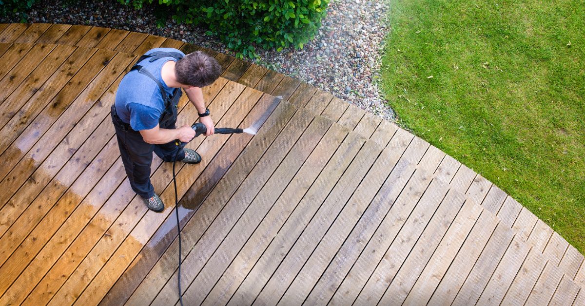 Person pressure washing a wooden deck with a high-pressure spray